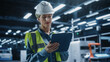 © Gorodenkoff - Beautiful Caucasian Female Engineer Standing In Factory Hall, Using Tablet Computer at Industrial Machinery Manufacturing Facility. Specialist Using Online Software to Program Robots on Assembly Line.