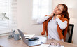 © NAMPIX - A tired young woman stretches her neck and shoulders to relieve stress and tension while working at her home office desk.