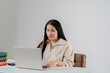 © pichet - Young woman with long black hair working on laptop at a desk with books in a bright indoor space focused on productivity and study habits
