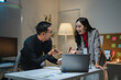 © PaeGAG - Asian businesspeople discussing and working late together using laptop in office at night