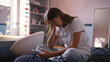 © Monkey Business - Depressed Teenage Girl Sitting On Bed At Home Looking At Mobile Phone With Head In Hands