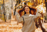Smiling young woman with curly hairstyle enjoys the autumn weather in the forest with the yellow leaves at sunset
