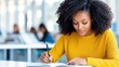 © mashimara - A beautiful black woman is focused on writing in a notebook, possibly in a classroom setting.