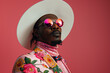 © apimagine - Modern fashion portrait of a man wearing a hat and an elegant suit with a floral print, paired with sunglasses in vivid, bright pink tones.