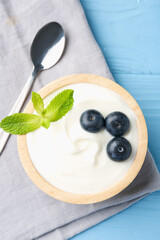 Wall Mural - tasty yoghurt with blueberries and mint in bowl on light blue wooden table, top view
