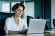 © Mselected - Professional woman working diligently on laptop in modern office environment