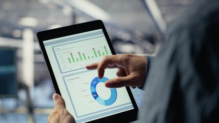 Close up of data center employee checking infrastructure diagnostics graphs on tablet screen. IT specialist on industrial platform in server room examining data charts during system audit, camera B