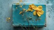 © Cuballe - Antique Teal Book Decorated with Yellow Flowers on Concrete