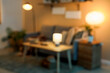 © Pixel-Shot - Blurred view of dark living room with glowing lamps, sofa and table at night