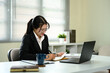 © Prathankarnpap - Businesswoman writing notes in a planner while working on her laptop in a modern office