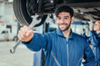 © Exnoi - Male mechanic in blue uniform extending wrench toward viewer, showing trustworthiness, professional service, and quality repair in automotive maintenance industry.
