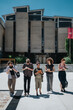 © qunica.com - A diverse group of students and their professor walking in front of a university building, carrying devices and notebooks.