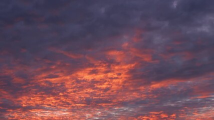 Wall Mural - A stunning sunrise time-lapse captures fiery orange clouds glowing against deep purple skies, as morning light spreads, revealing the vivid, dramatic beauty of nature’s awakening sky. Timelapse.
