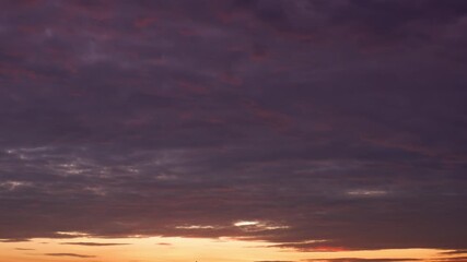 Wall Mural - A sunset timelapse captures dark clouds draped across the sky, glowing with deep red and orange at the horizon, as fading light paints a dramatic yet peaceful scene in nature’s evening display.
