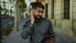 © Krakenimages.com - Young hispanic man with glasses using tablet on urban street, expressing curiosity and focus under soft daylight.