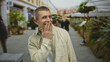 © Krakenimages.com - Caucasian man smiling playfully on a vibrant outdoor street with greenery and people in the background, combining humor and casual urban life with a sunny atmosphere.