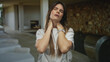 © Krakenimages.com - Young hispanic woman with long hair in a white shirt appears to feel neck discomfort in a modern indoor hotel setting.