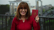 © Krakenimages.com - Senior woman holding a mexican passport smiles confidently in front of ancient roman ruins under a bright outdoor sky, blending cultural identity and historical exploration.