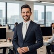 © klince - Confident Businessman in Modern Office Setting Smiling Brightly with Skyscrapers Visible Through Windows Creating a Professional Ambiance