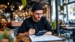 © Huzaifa - Man with beanie and glasses sitting at a table using a tablet and pen in a cafe environment indoors