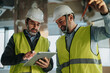 © qunica.com - Construction team collaborating on plans using a tablet, wearing safety vests and helmets, symbolizing planning and teamwork in an industrial setting.
