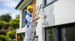 © Item.io - A construction worker in a hard hat is painting the exterior wall of a modern house while standing on a ladder.