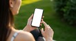 © Abimusa Gallery - Over the shoulder view of a woman holding a smartphone with a blank white screen in a park