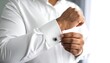 © can - Man prepares his elegant white shirt with sleek, square-shaped cufflinks