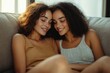 © Olya - Two young women sitting closely together on a couch with warm smiles and closed eyes sharing an intimate and peaceful moment