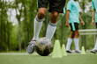 © Seventyfour - Teenager boys practicing soccer dribbling skills on outdoor field, focusing on controlling ball around training cones, legs and lower bodies visible, teammates standing in background