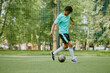 © Seventyfour - Teenage boy dribbling soccer ball on outdoor field, focusing on footwork during practice session, netted goal and green trees visible in background, athletic movement captured