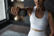 © DragonImages - Middle aged Caucasian woman exercising indoors, holding dumbbell with outstretched arm, wearing sportswear, focusing on strength training, partial face visible, blurred background