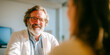 © Kos - A smiling doctor with glasses and a beard sits at a desk, wearing a white coat. Soft natural light illuminates the room, creating a welcoming atmosphere.