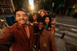 © bernardbodo - Group of happy young friends taking photo of themselves on city street at sunset