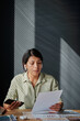 © TrueFrame Collective - Serious businesswoman in wireless headphones reading contract at her workplace at office