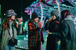 © qunica.com - Friends gather at a vibrant amusement park, enjoying treats and winter festivities. The scene depicts friendship, and joyful moments amid holiday lights and a lively atmosphere during the season.