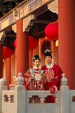 Traditional dressed couple posing in a historical architectural setting with red lanterns Chinese word means lanterns.