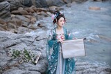 A woman in traditional attire holding a scroll by the water's edge Chinese word means scroll.