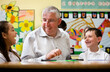 © track5 - Teacher and primary school pupils laughing together. A male teacher sits with a boy and a girl at a classroom table, sharing a laugh and enjoying a moment during the school day. From an image series.