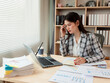 © ArLawKa - Asian businesswoman holding pen and analyzing financial documents while working on laptop computer at desk in office.
