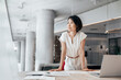© Stock 4 You - Thoughtful asian professional financial analyst specialist business lady working on laptop pc. Middle eastern woman investor dreaming standing standing at computer in modern office. Copy space