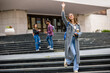 © Mediteraneo - Female Student Waving with Books and Coffee on College Campus