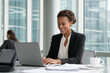 © The Pixel Store - Smiling businesswoman working on laptop in modern office silhouette