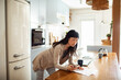 © Marko Geber - Woman reviewing utility bill at home while using laptop in bright kitchen