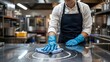 © Pixels Stock - Professional chef wearing blue gloves meticulously cleaning a stainless steel kitchen counter with a blue cloth ensuring hygiene and cleanliness in a commercial restaurant