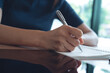 © tippapatt - Closeup, woman hand with a pen writing on paper notebook with digital tablet on office table, business planning. Student doing homework, writing on notepad at home