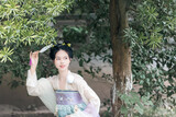 Young woman in traditional attire holding a fan amidst greenery Chinese word means fan.