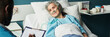 © Mediaphotos - Header of senior Caucasian woman lying in hospital bed wearing oxygen tube, looking at Black man healthcare professional holding clipboard, receiving medical care in clinical setting
