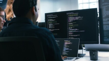 Two Software Developer, Programmer discussing, explaining to colleague working on code, application software development project using desktop computer, work together in co-working office space.