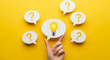 © Inspire Shots Hub - Hand holding illuminated bulb amidst question mark speech bubbles on yellow background, symbolizing problem-solving, idea generation, and finding answers